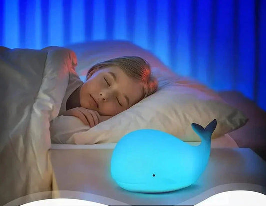 Child sleeping with a whale-shaped night light on a bed