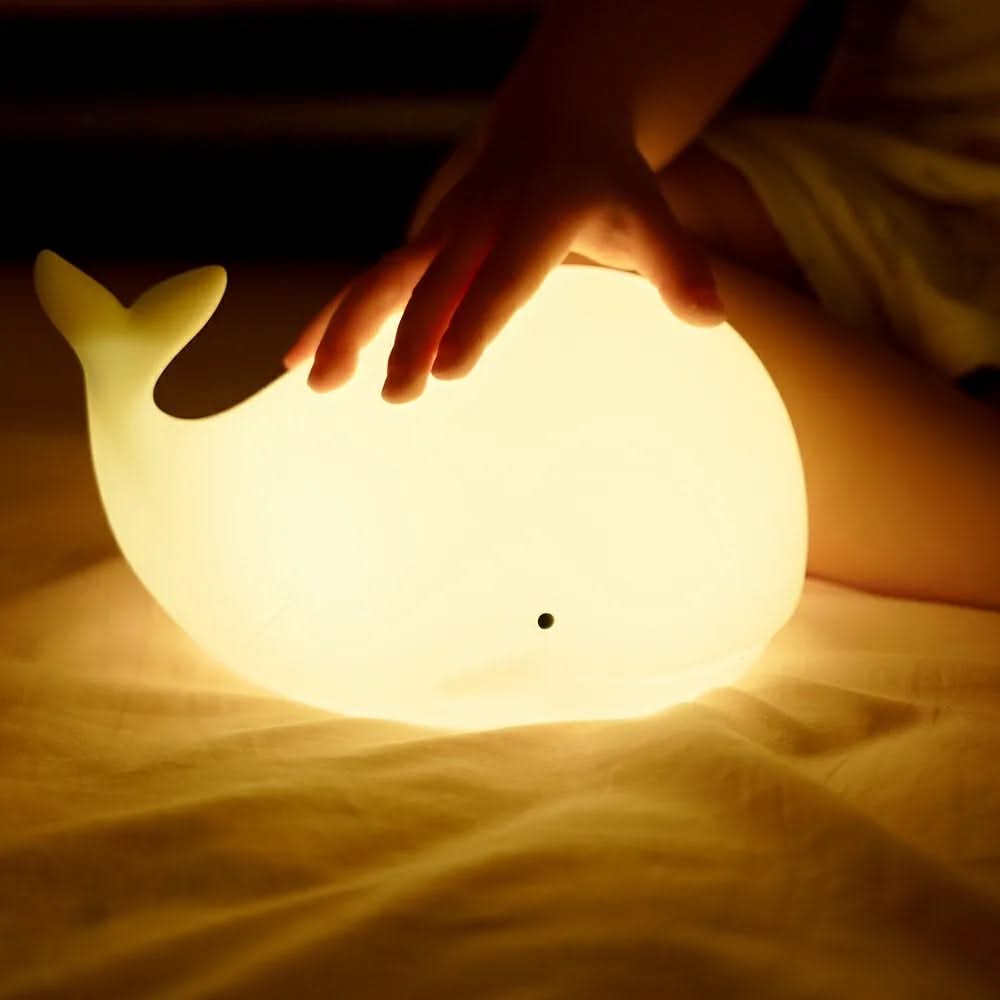 Whale-shaped night light being held by a child's hand on a soft surface