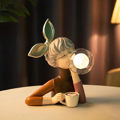 Decorative lamp shaped like a person with leaf hair, holding a cup and a light bulb, on a table.