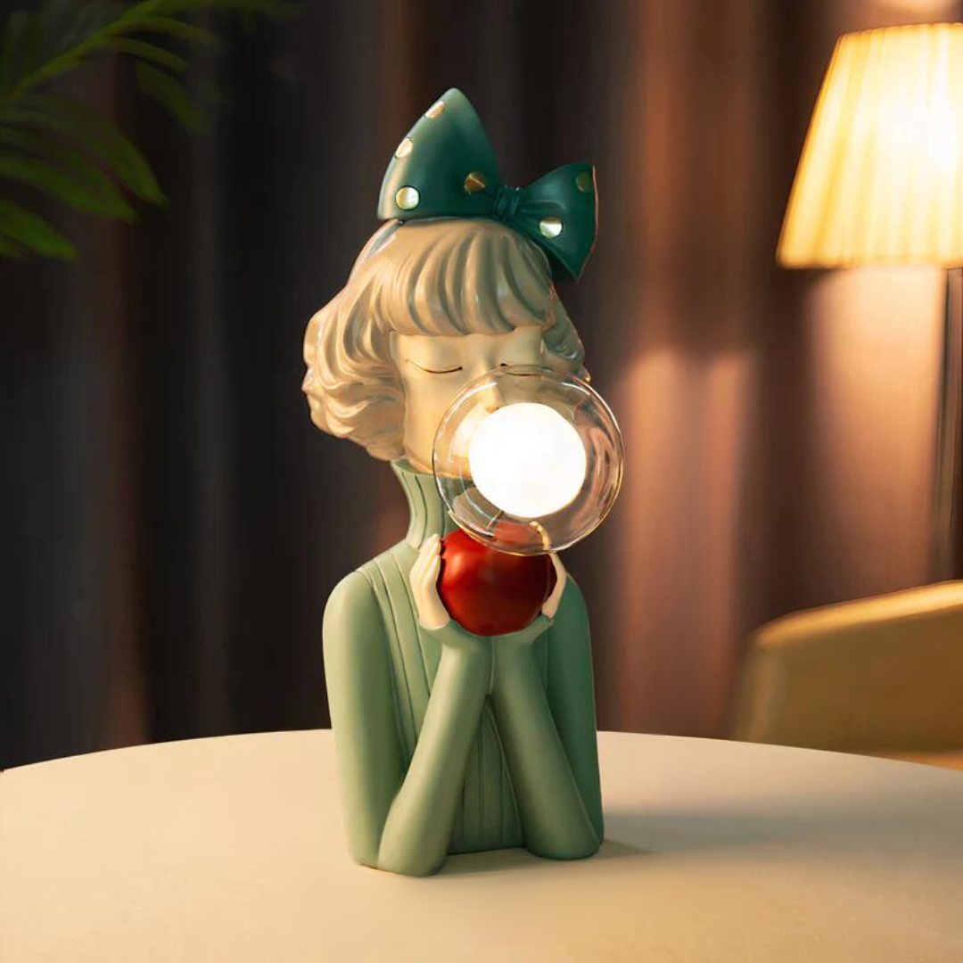 Decorative lamp shaped like a girl with a bow and apple, emitting light.