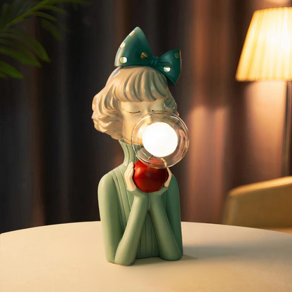 Decorative lamp shaped like a girl with a bow and apple, emitting light.
