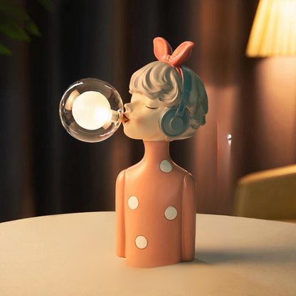 Decorative lamp shaped like a girl blowing a bubble with a light bulb inside, on a blurred background.