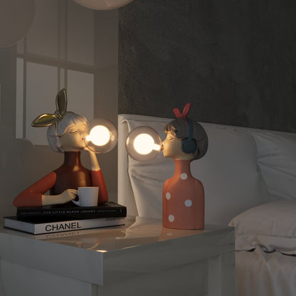 Two decorative lamps shaped like people on a table with books and a mirror in the background.