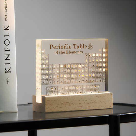 Light-up periodic table of elements on a wooden base with a book titled 'KINFOLK' in the background.
