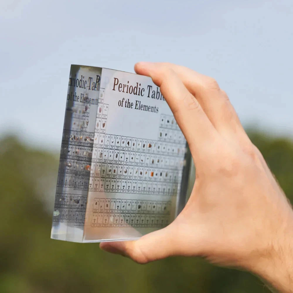 Josh & Tate - Elementa Periodic Table - Hand holding a transparent periodic table against a blurred natural background