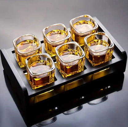 Set of six square glass shot glasses filled with a golden liquid on a black tray.