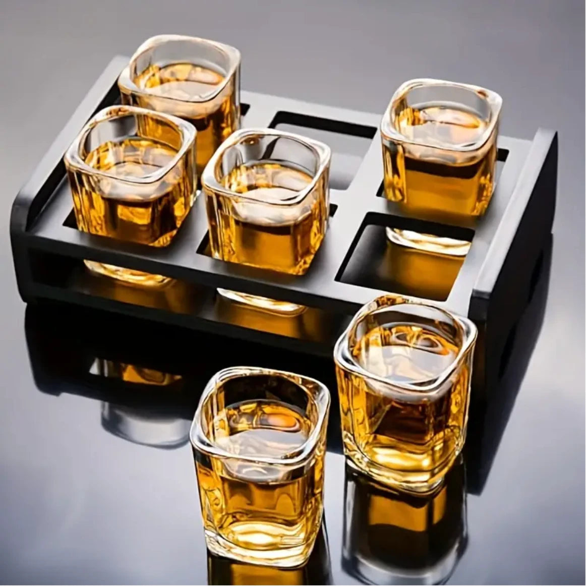 Six square glass shot glasses filled with a golden liquid on a black tray.