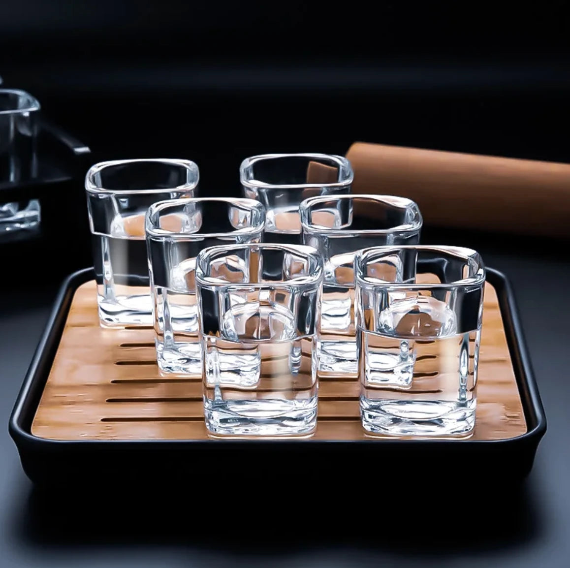 Set of clear glass tumblers on a wooden tray with a black rim.