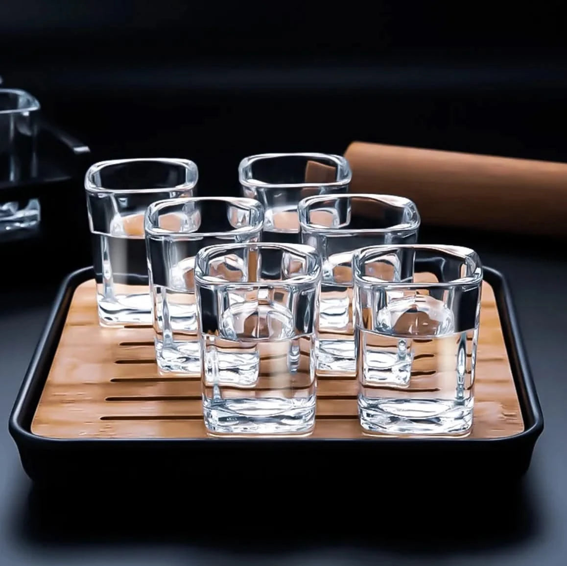 Set of clear glass tumblers on a wooden tray with a black rim.
