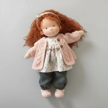 Doll with red hair wearing a pink knitted cardigan and floral dress on a gray background