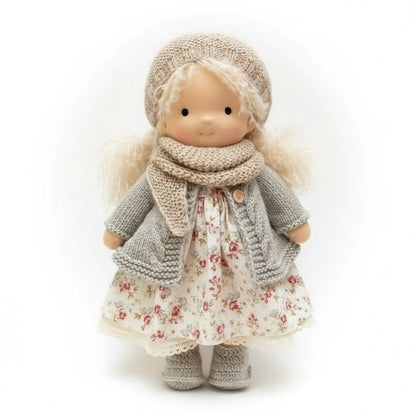 Toy doll wearing a floral dress, knitted coat, and hat on a white background