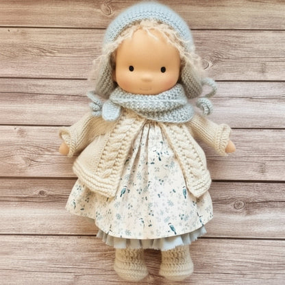 Doll wearing a knitted outfit with a floral dress on a wooden background