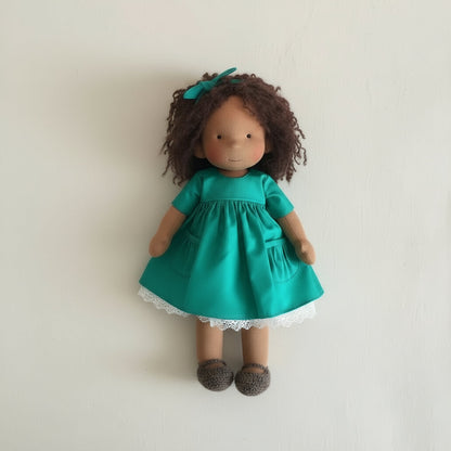 Doll wearing a green dress with a white lace trim on a plain background