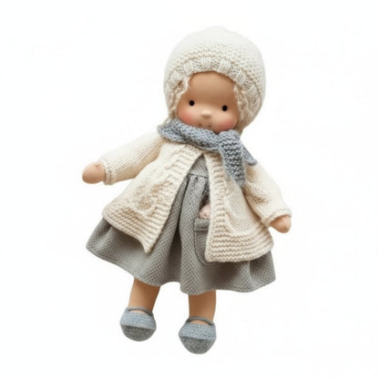 Doll wearing a knitted outfit with a coat, hat, and scarf on a white background