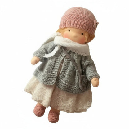 Doll wearing a gray knitted coat, white dress, and pink hat on a white background