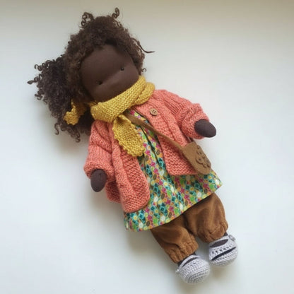 Doll wearing a pink coat, yellow scarf, and floral dress on a white background