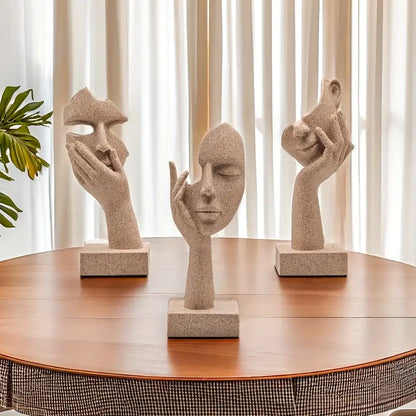 A set of three abstract figurines with a mask design on a table, showcasing a sandstone finish.
