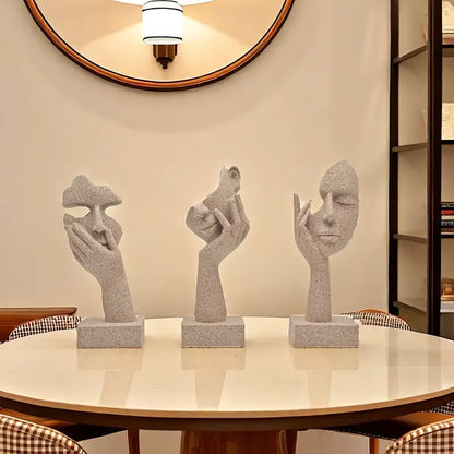 A set of three abstract figurines with a mask design on a table, showcasing a sandstone finish.