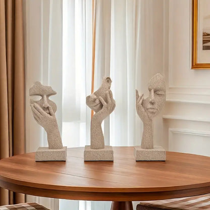 A set of three abstract figurines with a mask design on a table, showcasing a sandstone finish.