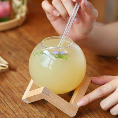 Josh & Tate - Floating Sphere Glass (16oz / 500mL) - Glass ball with yellow liquid and a straw on a wooden stand, held by a person.