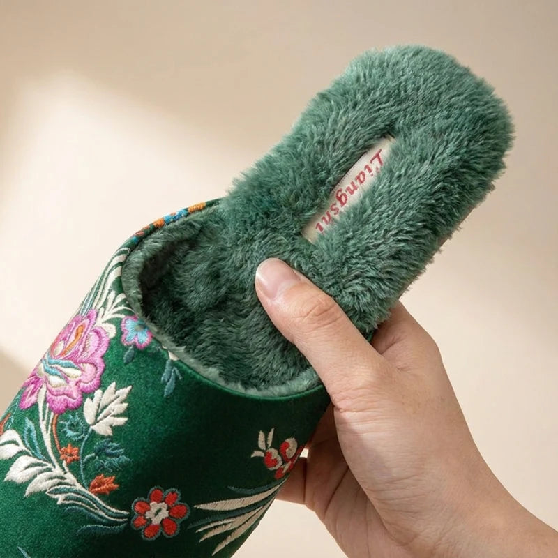 Josh & Tate - FloraStep™ Satin Fur-Lined Slipper - Green embroidered slipper with fluffy interior held by a hand against a beige background