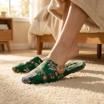 Josh & Tate - FloraStep™ Satin Fur-Lined Slipper - Person wearing green floral slippers on a carpeted floor with a bed in the background.