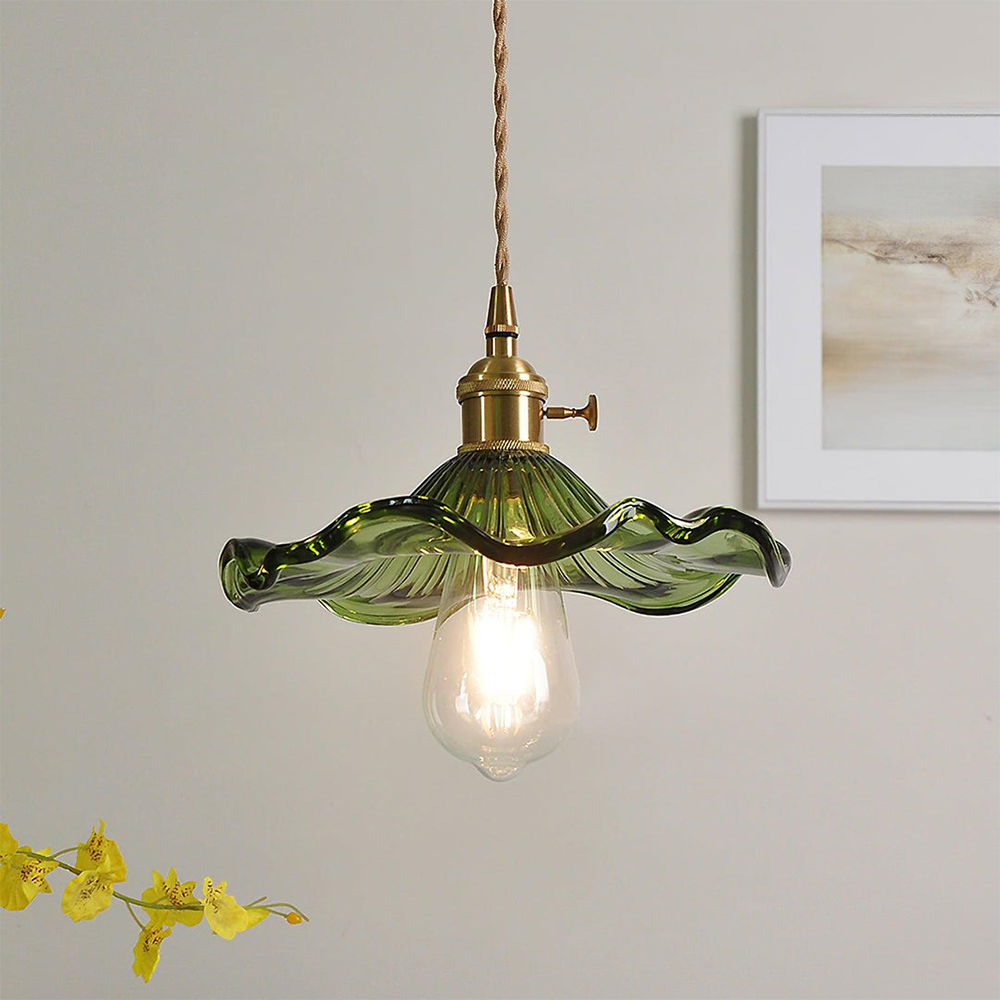 Green pendant light with brass fixture on a neutral wall with a framed picture and yellow flowers.