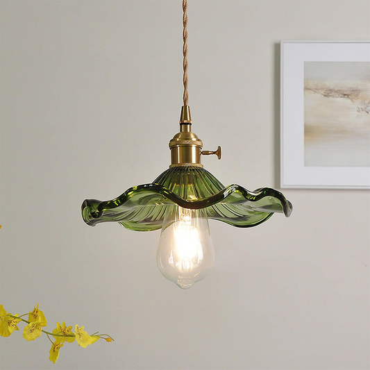 Green pendant light with brass fixture on a neutral wall with a framed picture and yellow flowers.