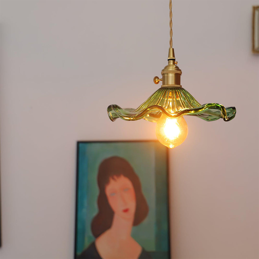 Green pendant light with a glowing bulb hanging against a neutral wall with a blurred portrait in the background.