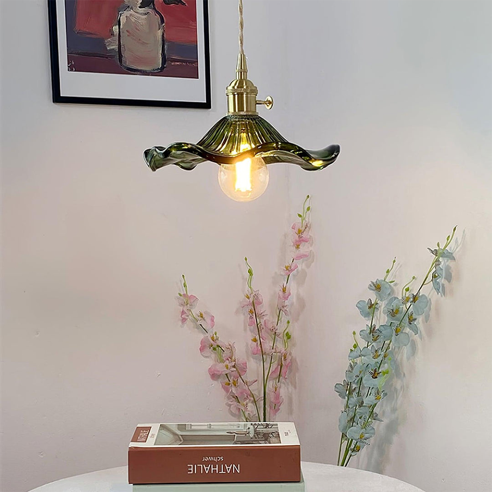 Decorative pendant light with a gold and green shade hanging above a table with books and flowers.