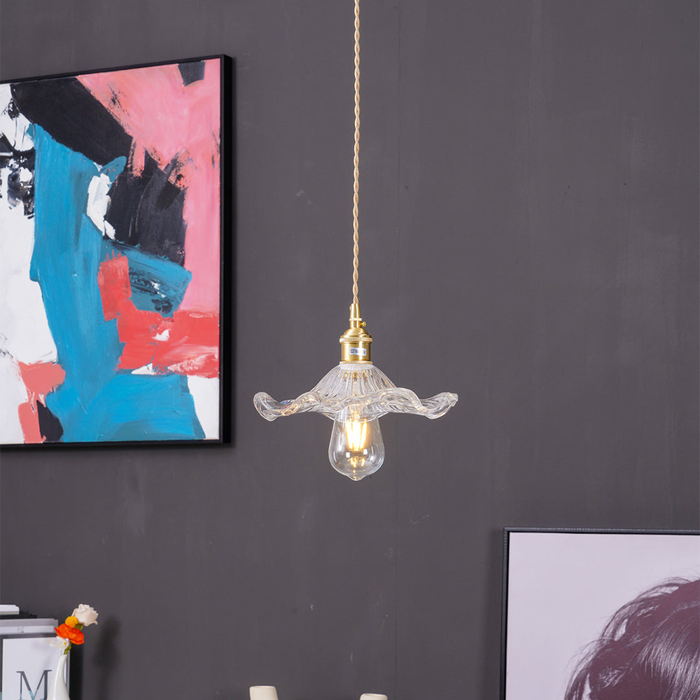 Glass pendant light with gold fixture hanging against a dark gray wall with abstract art.