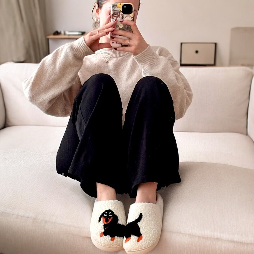 Person wearing white slippers with a dog design, sitting on a couch.
