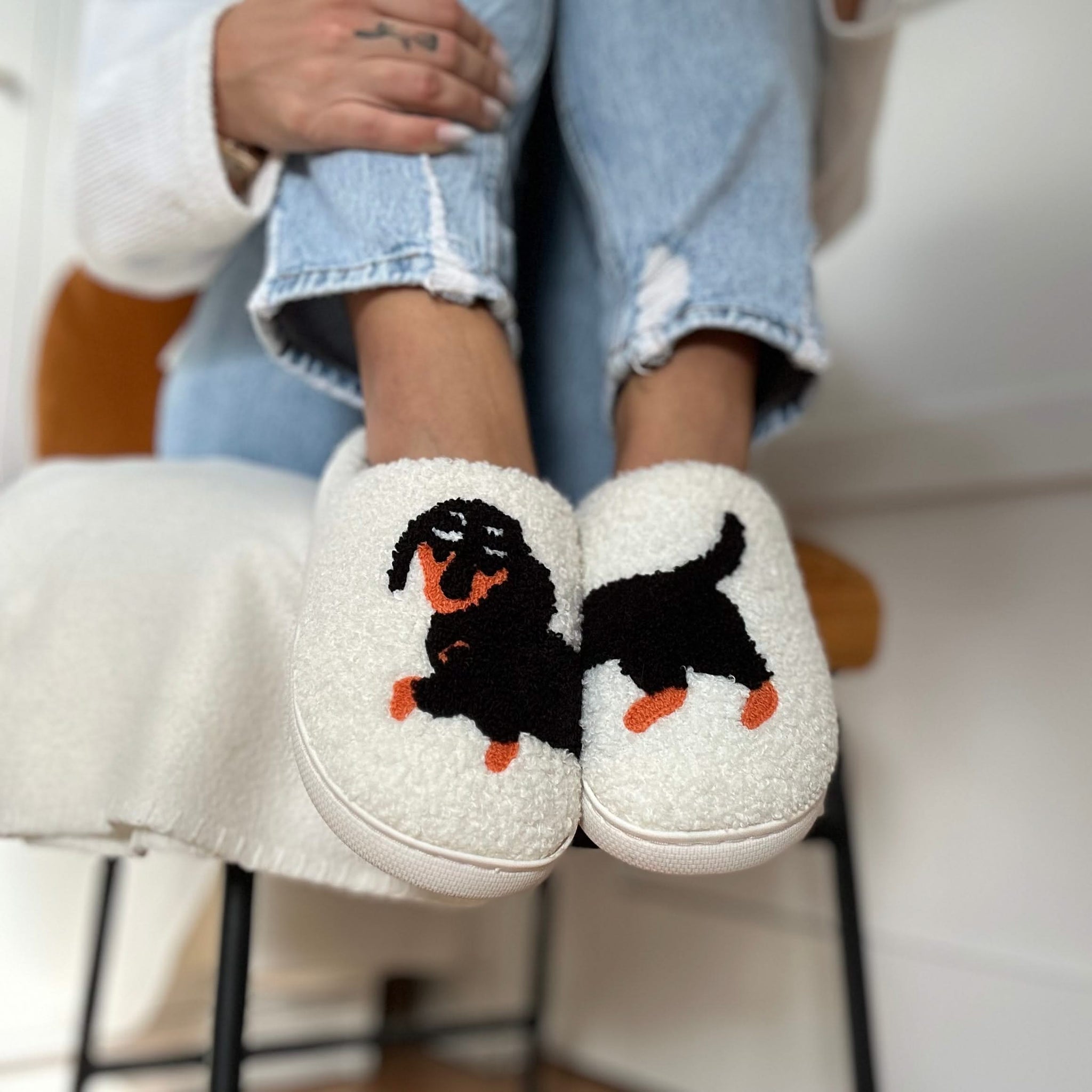 White slippers with a dog design worn by a person sitting on a chair.
