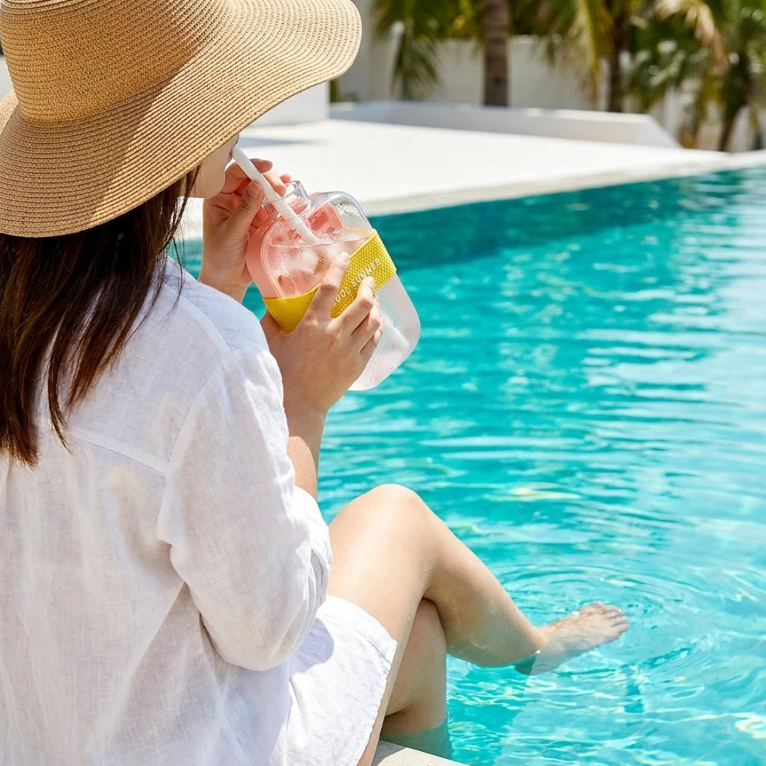 Josh & Tate - FrostPour™ 2-in-1 Ice Cube Tray & Drinking Bottle - Person in a straw hat and white dress by a pool, holding a drink with a lemon slice.