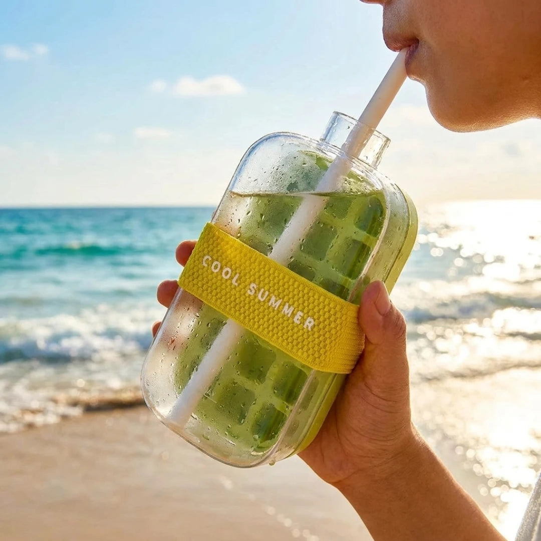 Josh & Tate - FrostPour™ 2-in-1 Ice Cube Tray & Drinking Bottle - Person holding a glass jar with a yellow band labeled 'Cool Summer' filled with a green drink on a beach.