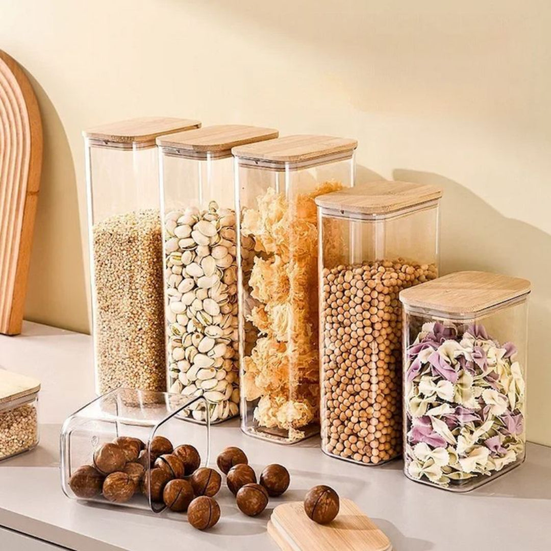 Set of glass storage jars with wooden lids containing various dry goods on a kitchen counter.