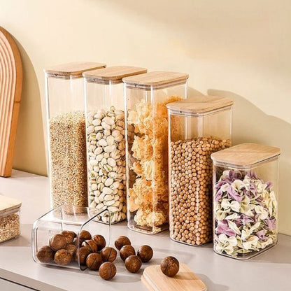 Set of glass storage jars with wooden lids containing various dry goods on a kitchen counter.
