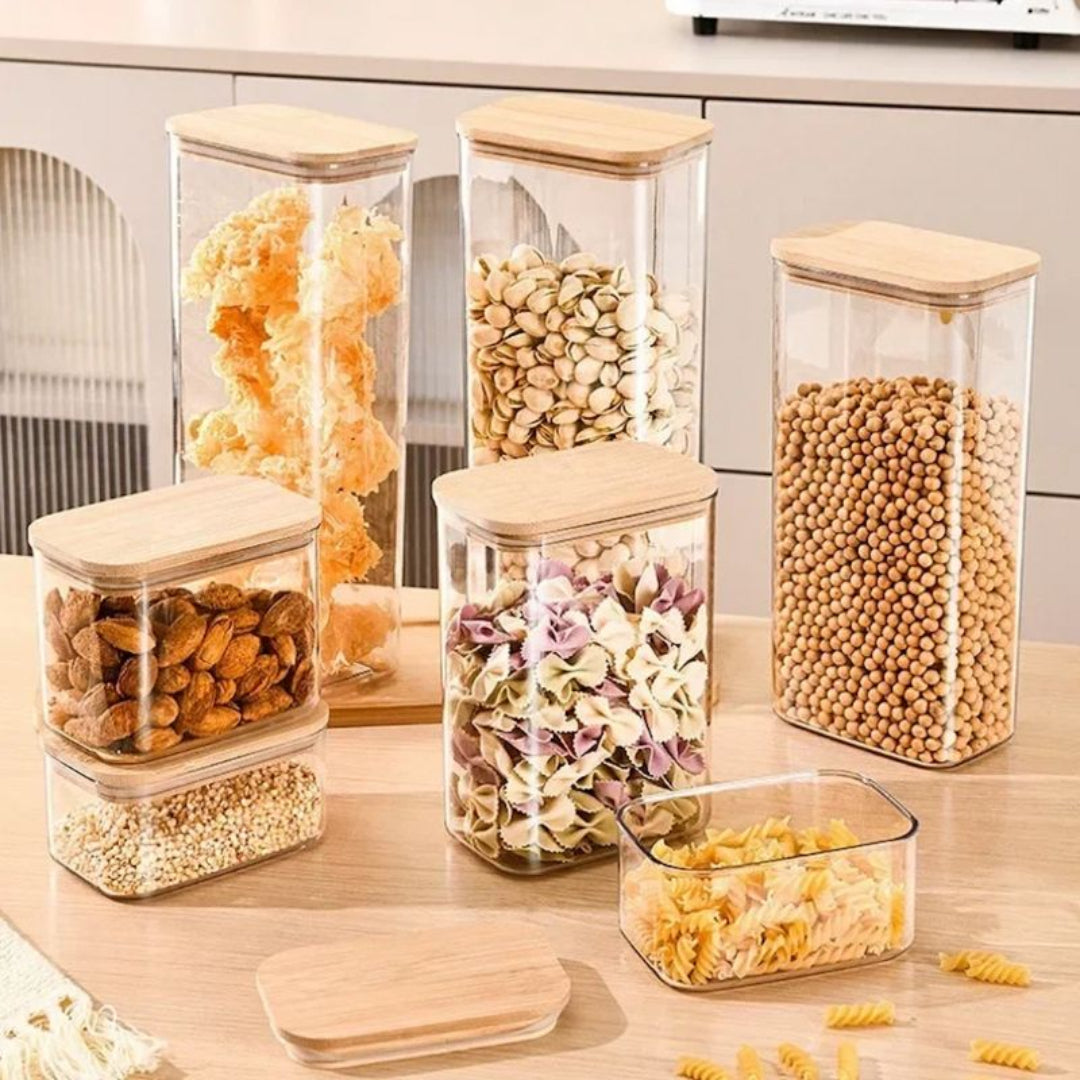 Set of glass storage jars with wooden lids containing various dry goods on a kitchen counter.