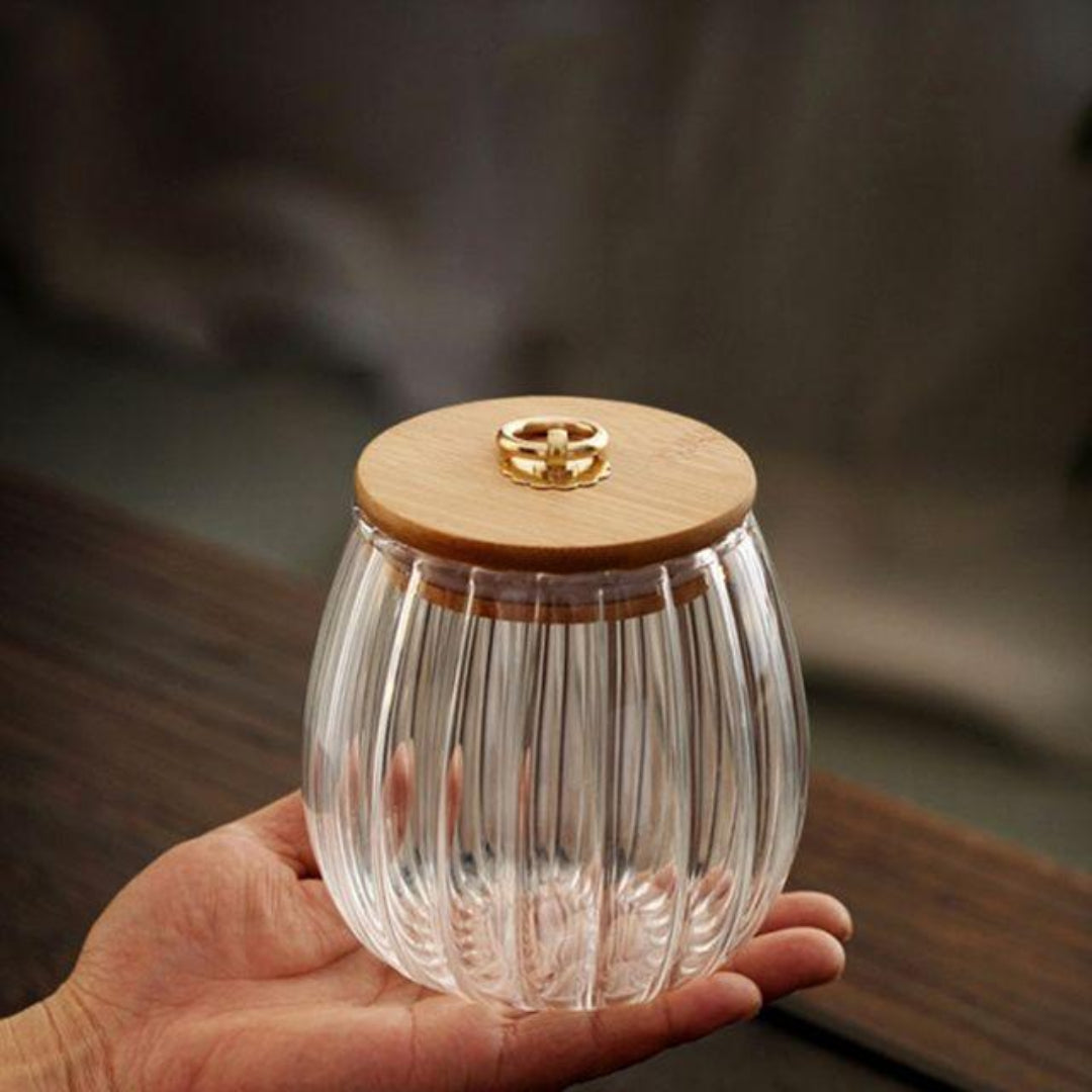 Clear glass container with wooden lid held in a hand against a blurred background