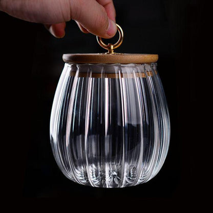 Clear glass container with wooden lid held by a hand against a black background