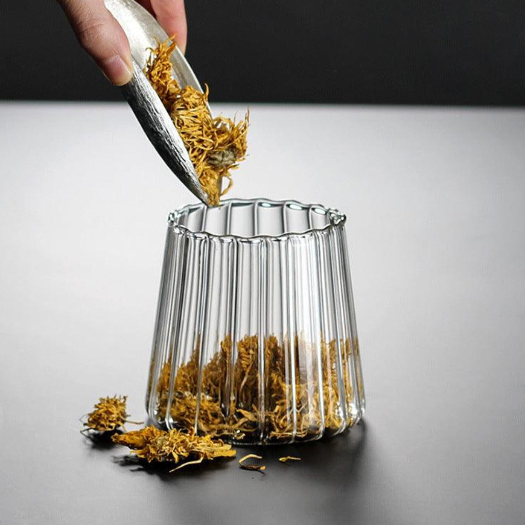 Hand using tongs to place yellow dried flowers into a clear glass vase on a gray background