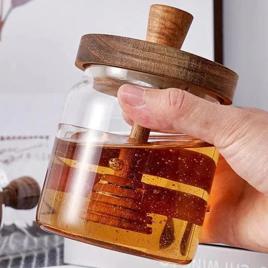Glass bottle with wooden lid filled with honey, held by a hand.