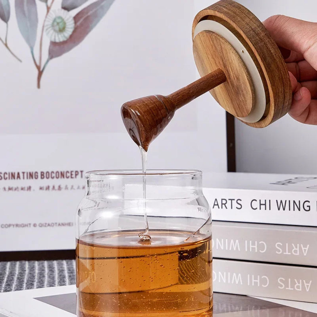 Wooden honey dipper drizzling honey into a glass jar with a blurred background.