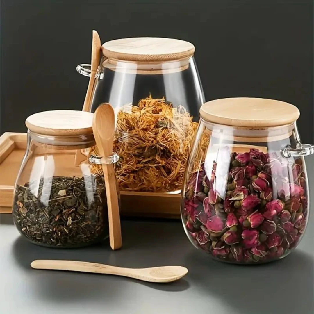 Josh & Tate - Glass Storage Jar with Spoon - Glass jars with wooden lids and spoons containing various dried herbs on a dark background