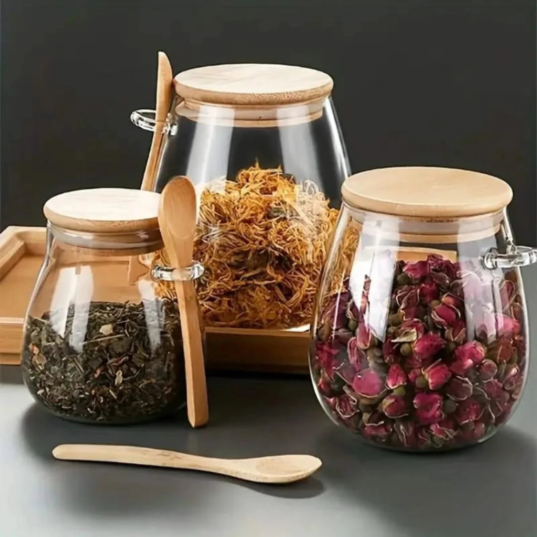 Josh & Tate - Glass Storage Jar with Spoon - Glass jars with wooden lids and spoons containing various dried herbs on a dark background