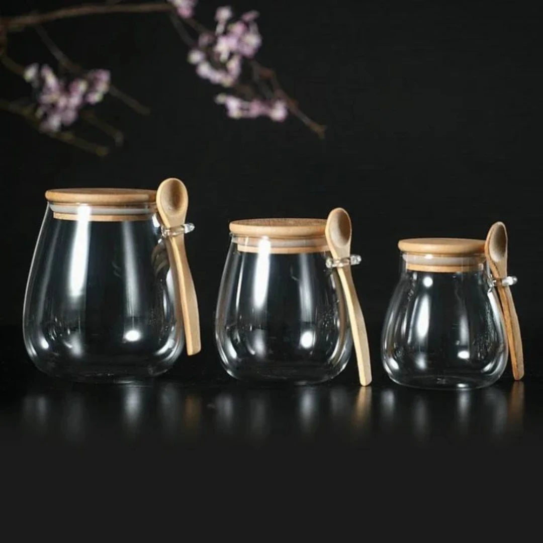 Josh & Tate - Glass Storage Jar with Spoon - Three glass jars with wooden lids and spoons on a dark background