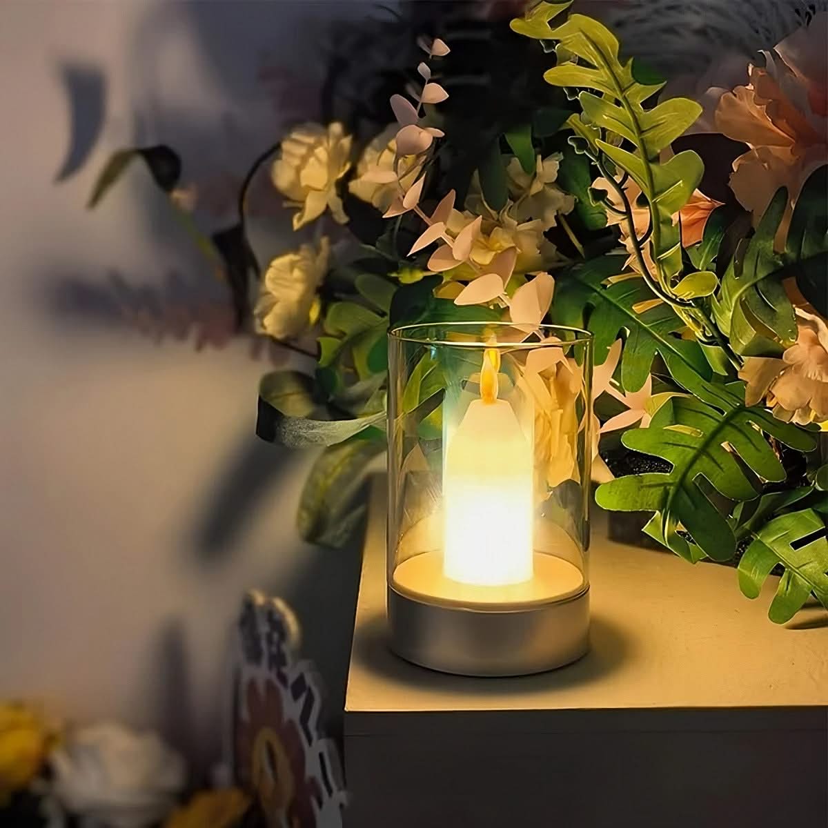 Candle in a glass holder on a table with plants in the background