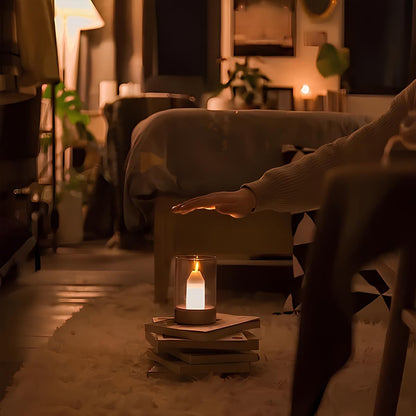 Person holding an outstretched hand towards a lit candle on a stack of books in a dimly lit room.