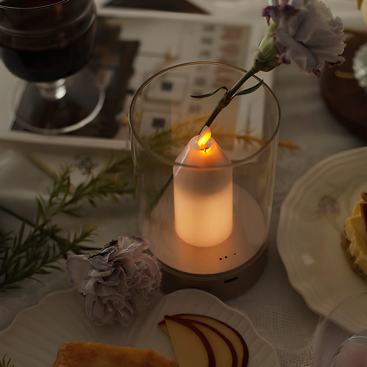 Candle in a glass holder on a table with food and flowers