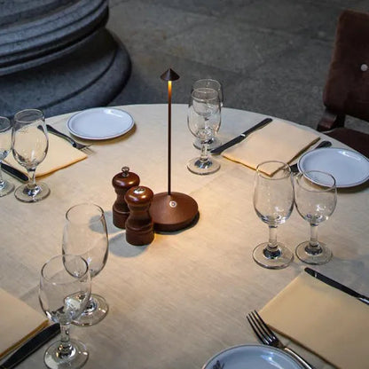 Dining table setup with wine glasses, plates, cutlery, and a small lamp.
